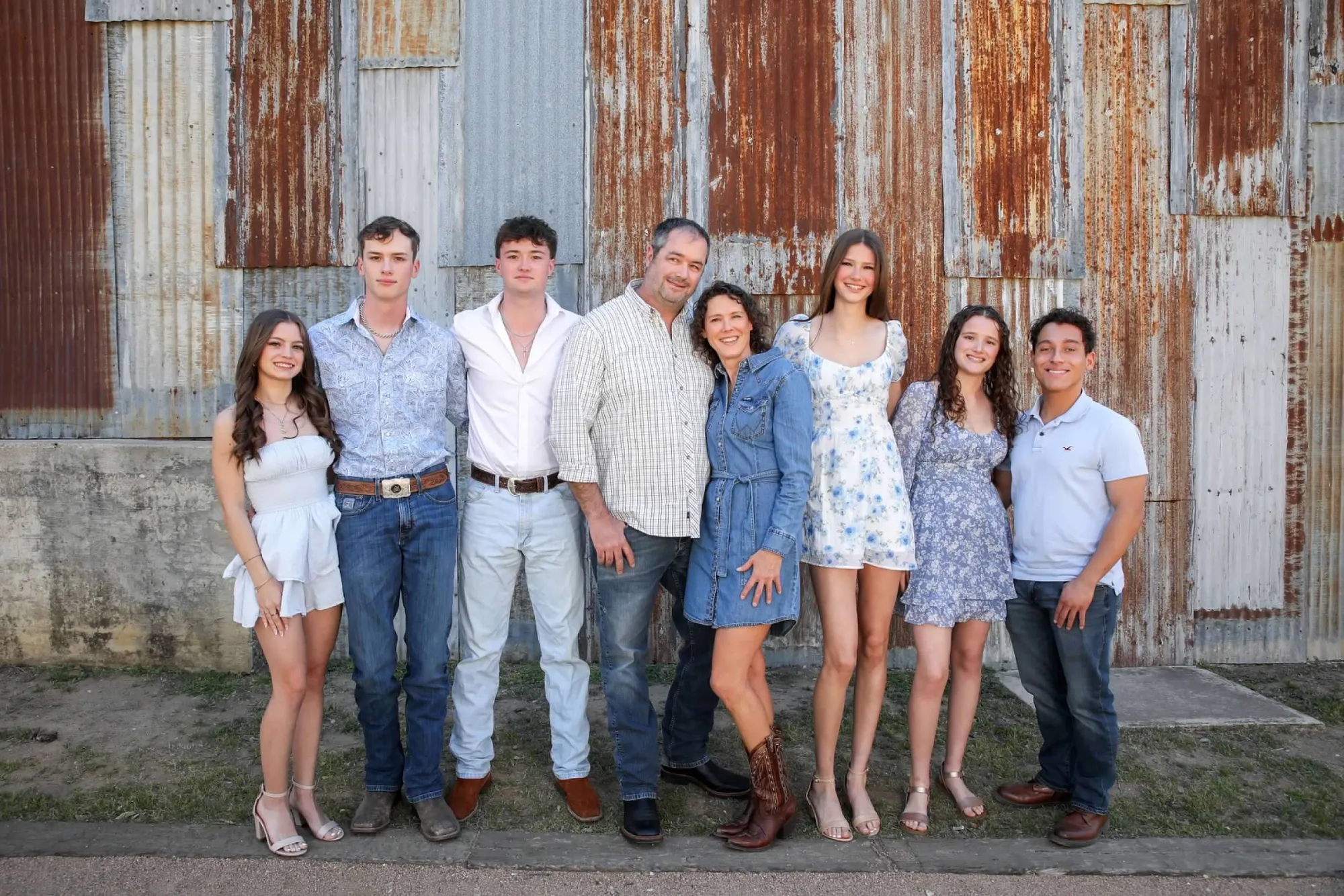 The Bowdoin family standing in front of a weathered tin barn wall at their ranch in La Vernia, Texas